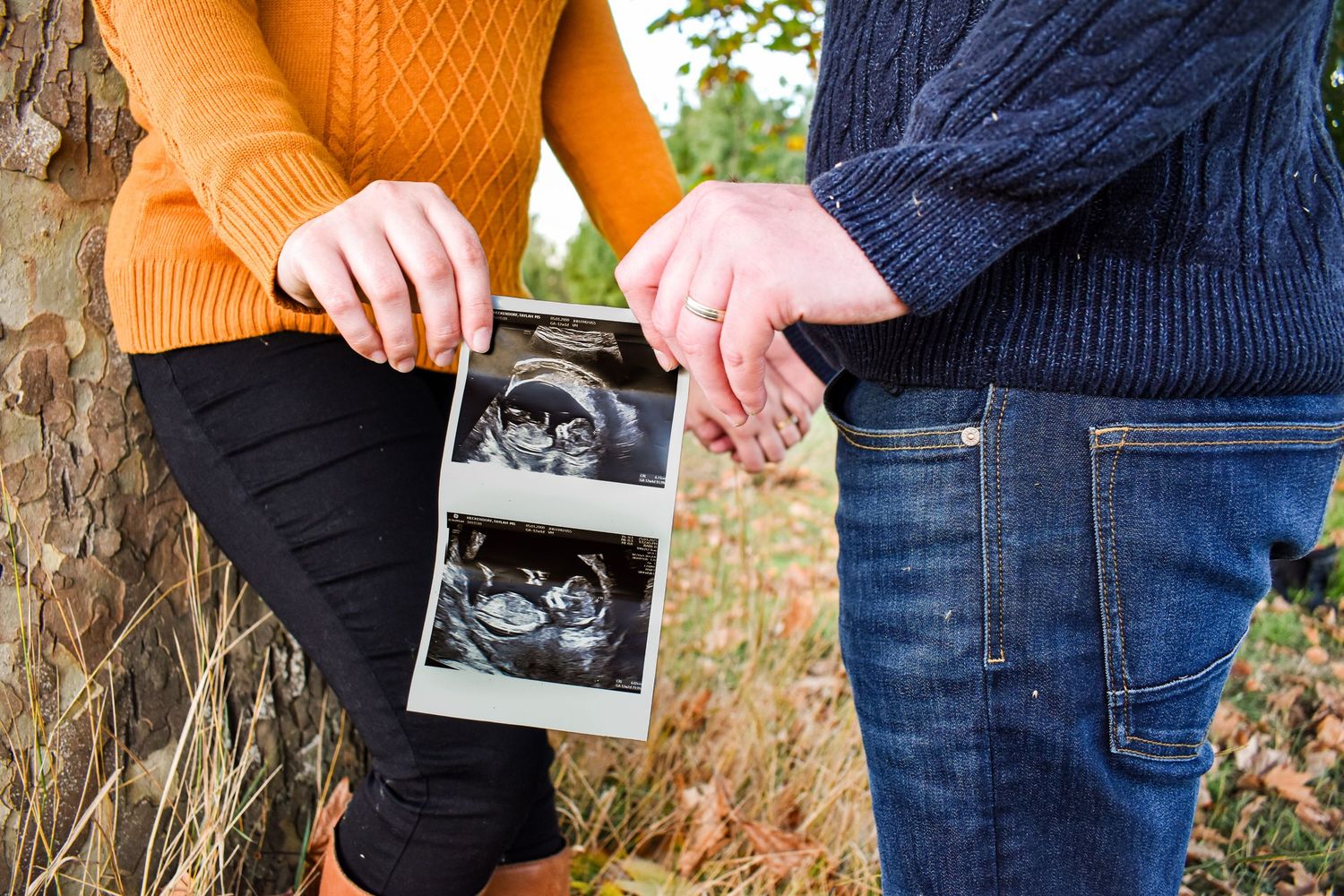 Couple's hands holding ultrasound photo against casual denim and sweater backdrop.