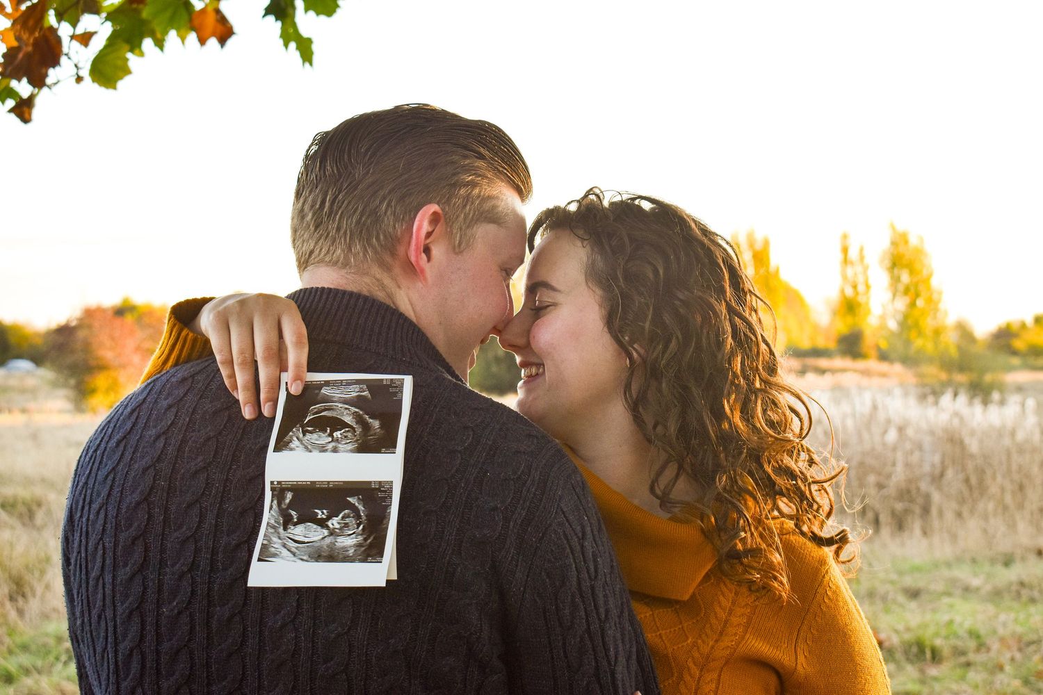 Couple holding ultrasound photo during autumn sunset session.