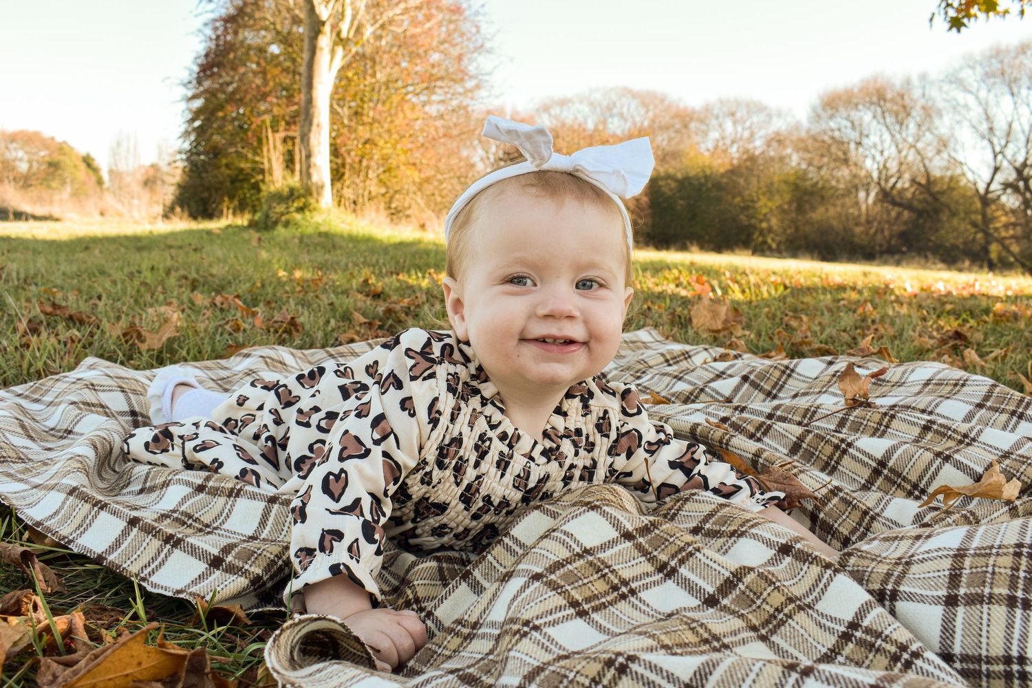 Family lying on plaid blanket during autumn outdoor photoshoot.