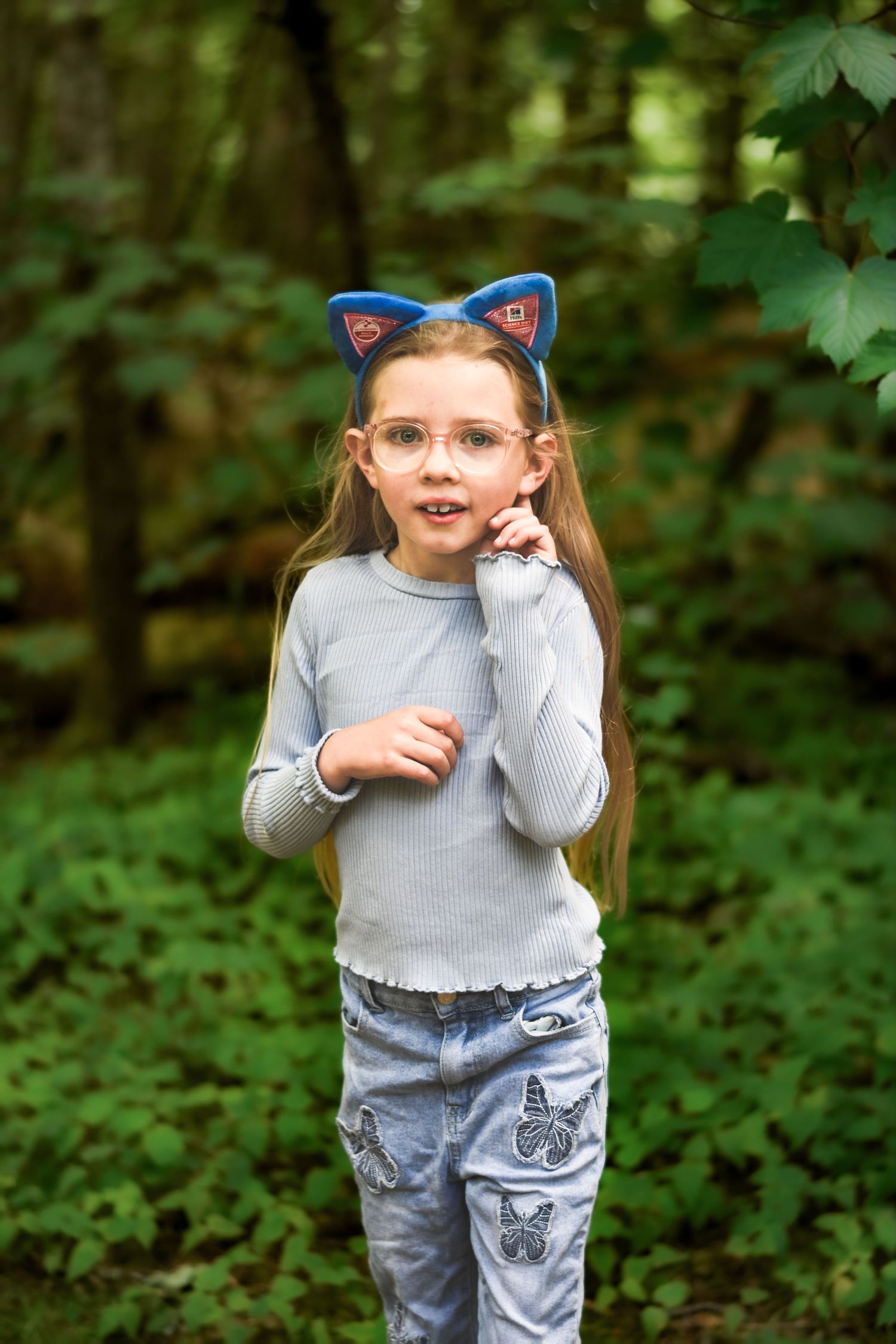 Playful sequence of a young child in casual wear and cat ears posing in a wooded setting.