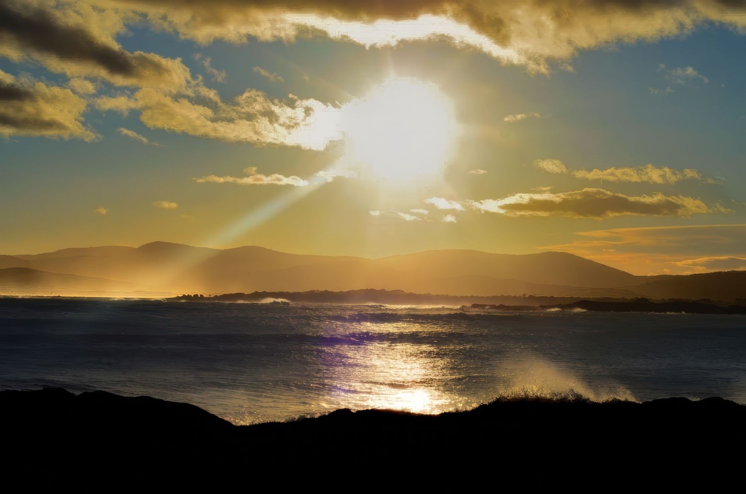 Dramatic sunrise over ocean horizon with golden clouds and sunburst.