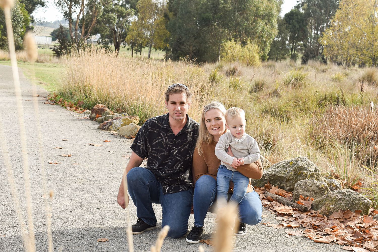 Family sitting together outdoors on a path surrounded by autumn foliage.