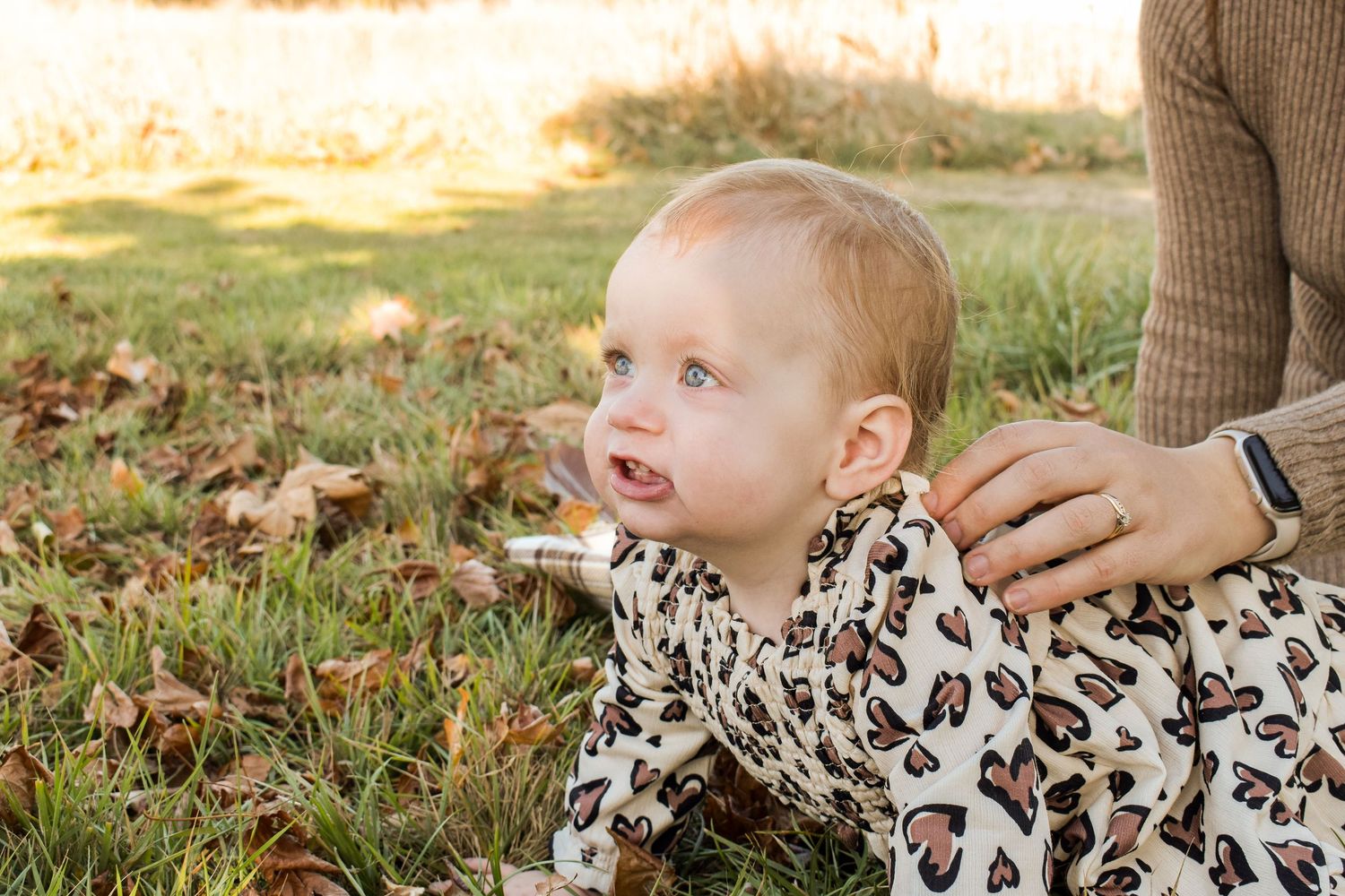 Young child playing in autumn leaves wearing leopard print outfit.