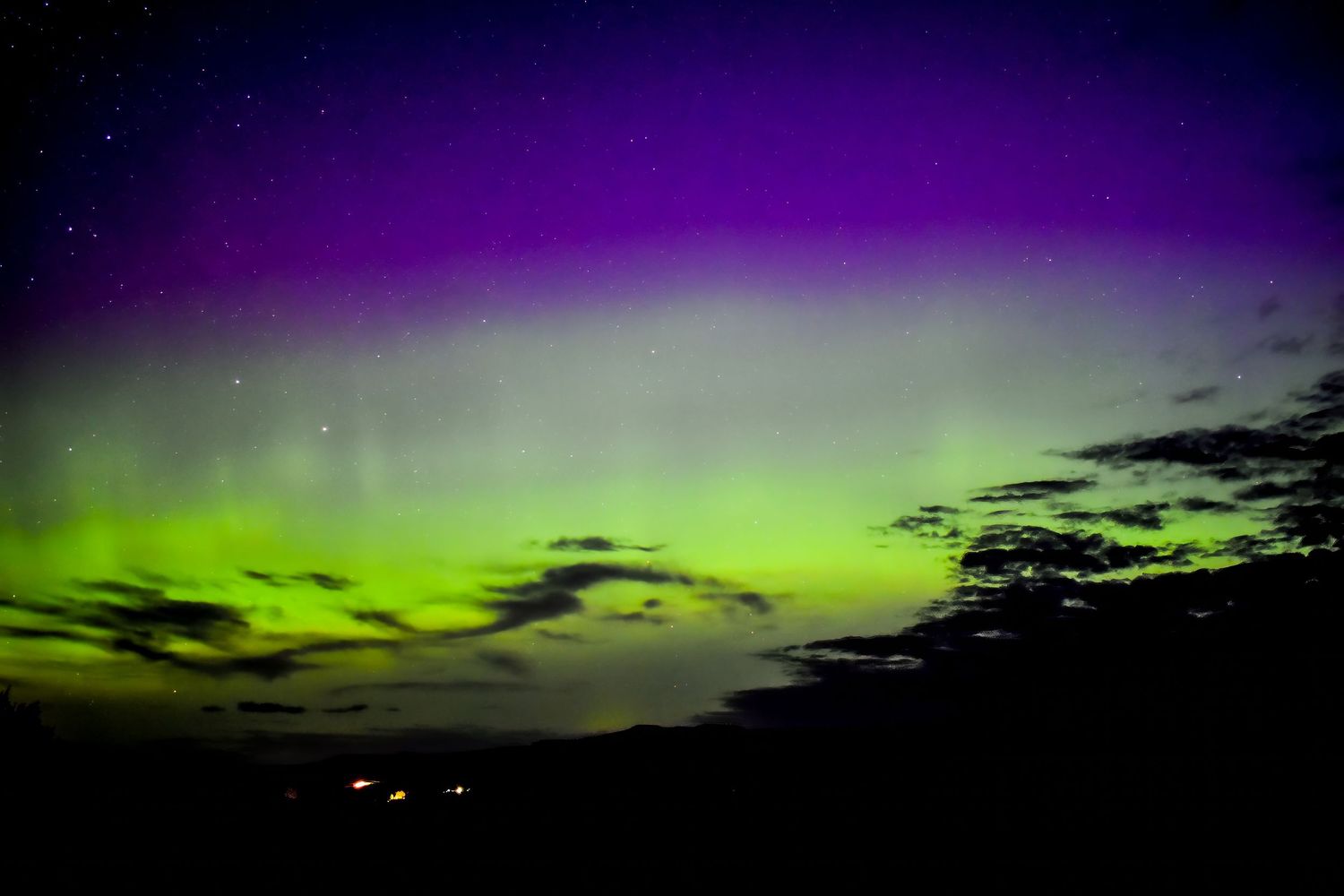 Aurora borealis creating a dramatic light show with green and purple colors over a dark landscape.