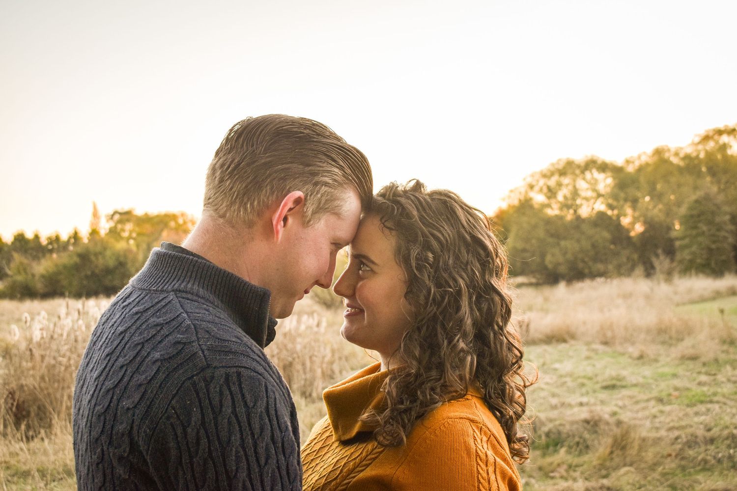 Couple sharing intimate moment during golden hour in field setting.
