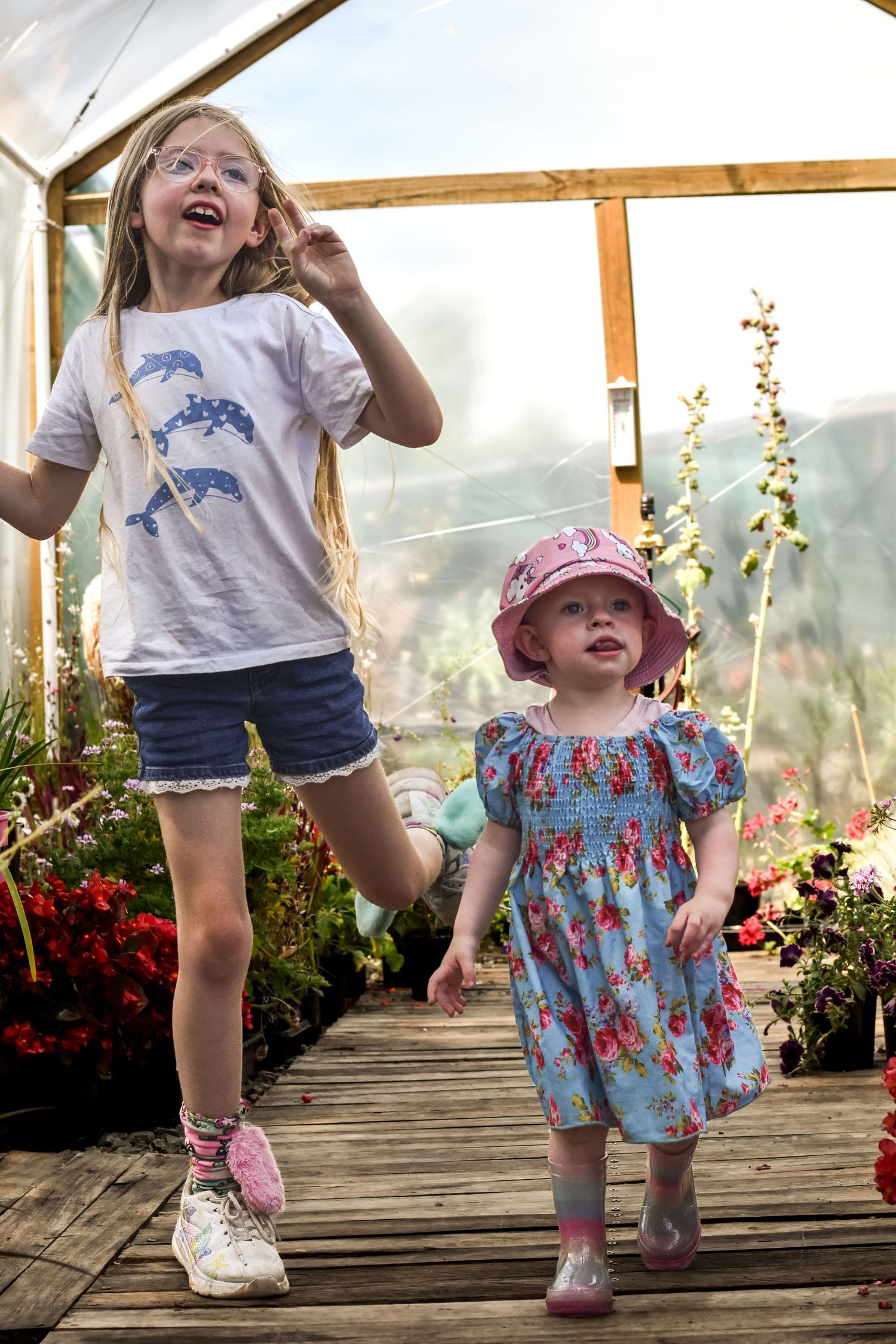 Two children playing and jumping on a wooden deck surrounded by flowers.