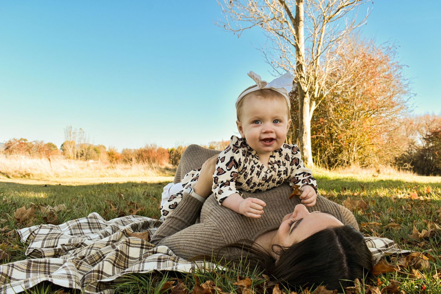 A cozy plaid blanket spread out under bare autumn trees during golden hour.