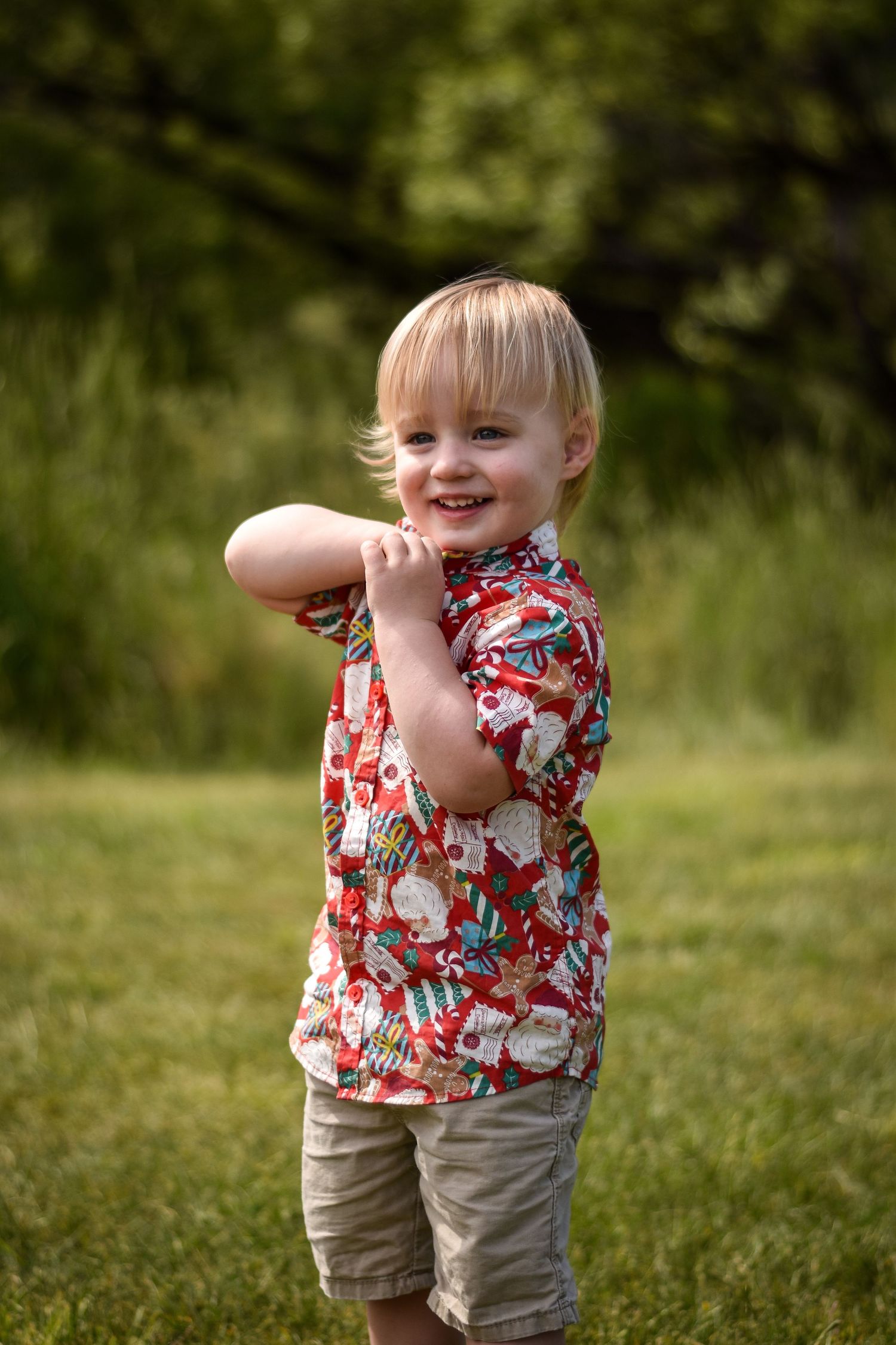 Small child in floral shirt and khaki shorts playing outdoors in grass.