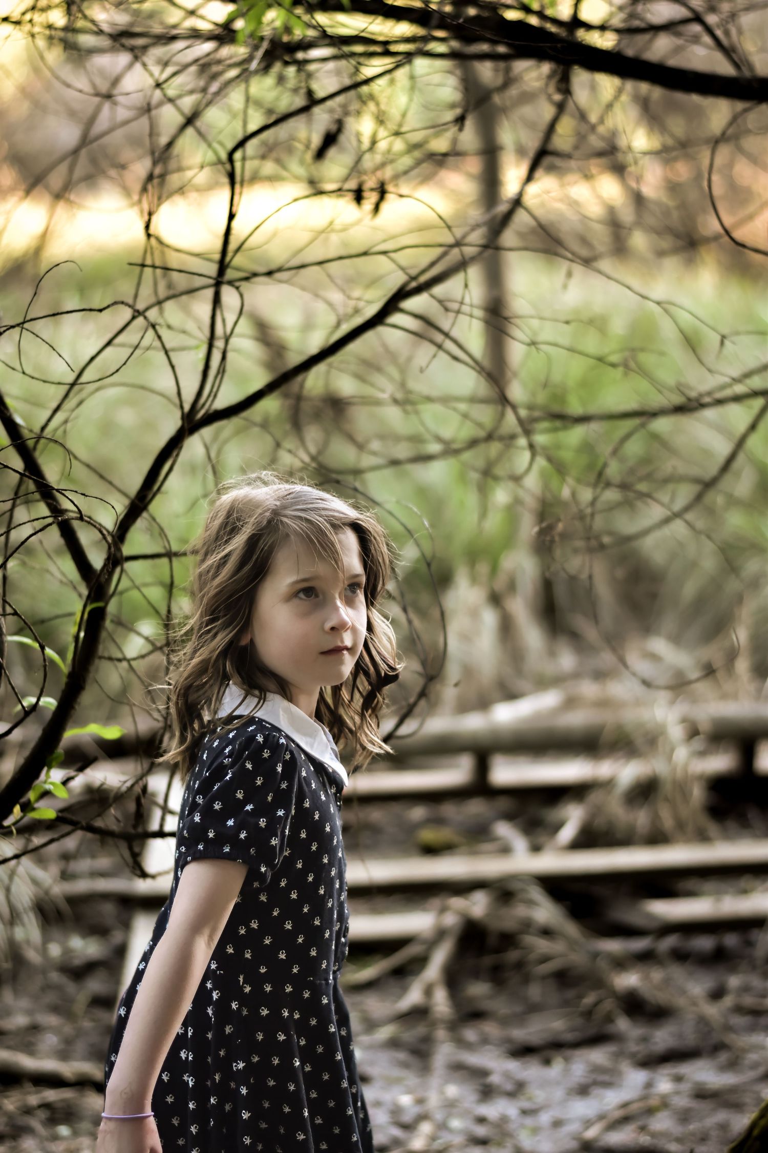 Child in polka dot dress exploring a wooded area with fallen branches.