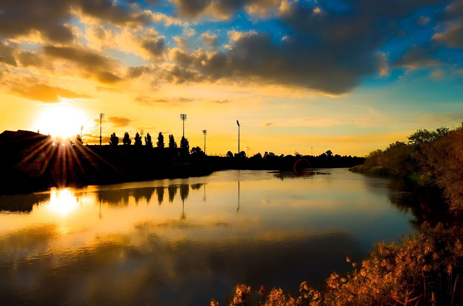 Panoramic sunset silhouette of harbor with boats and dramatic orange sky.