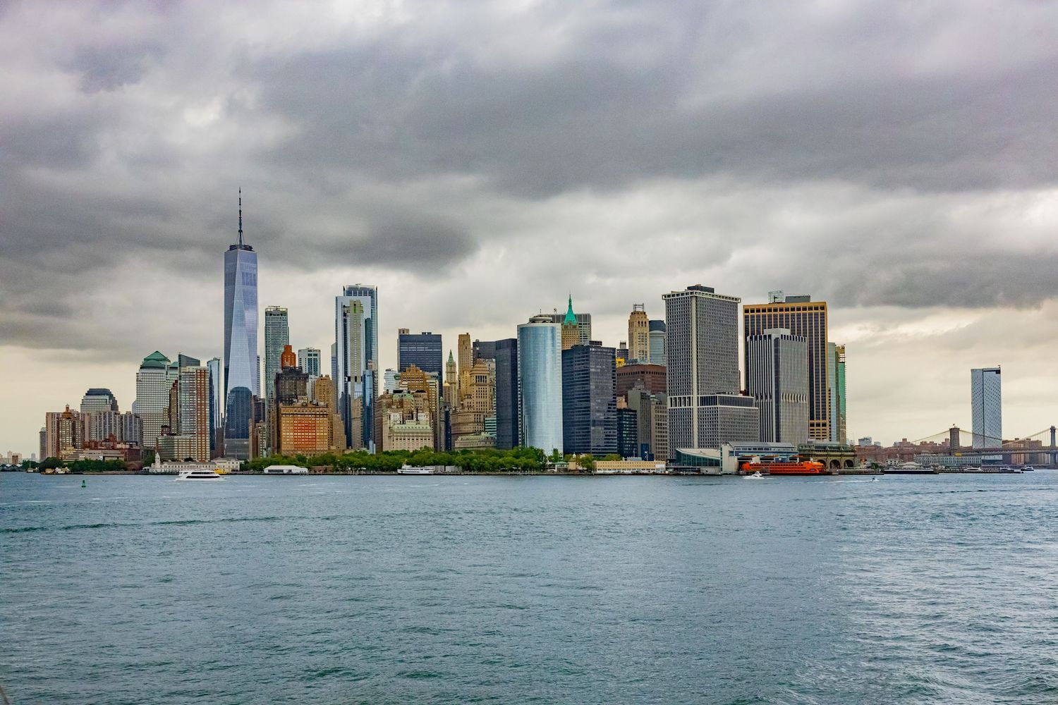 Lower Manhattan skyline with One World Trade Center seen from the water under overcast skies.