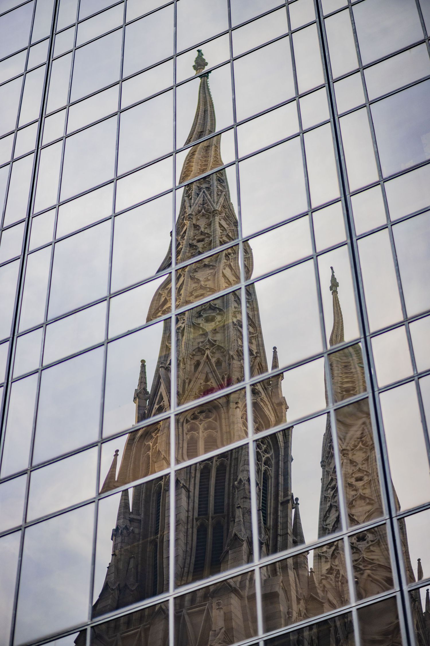 Gothic cathedral spire reflected in modern glass skyscraper windows creating a stunning architectural contrast.