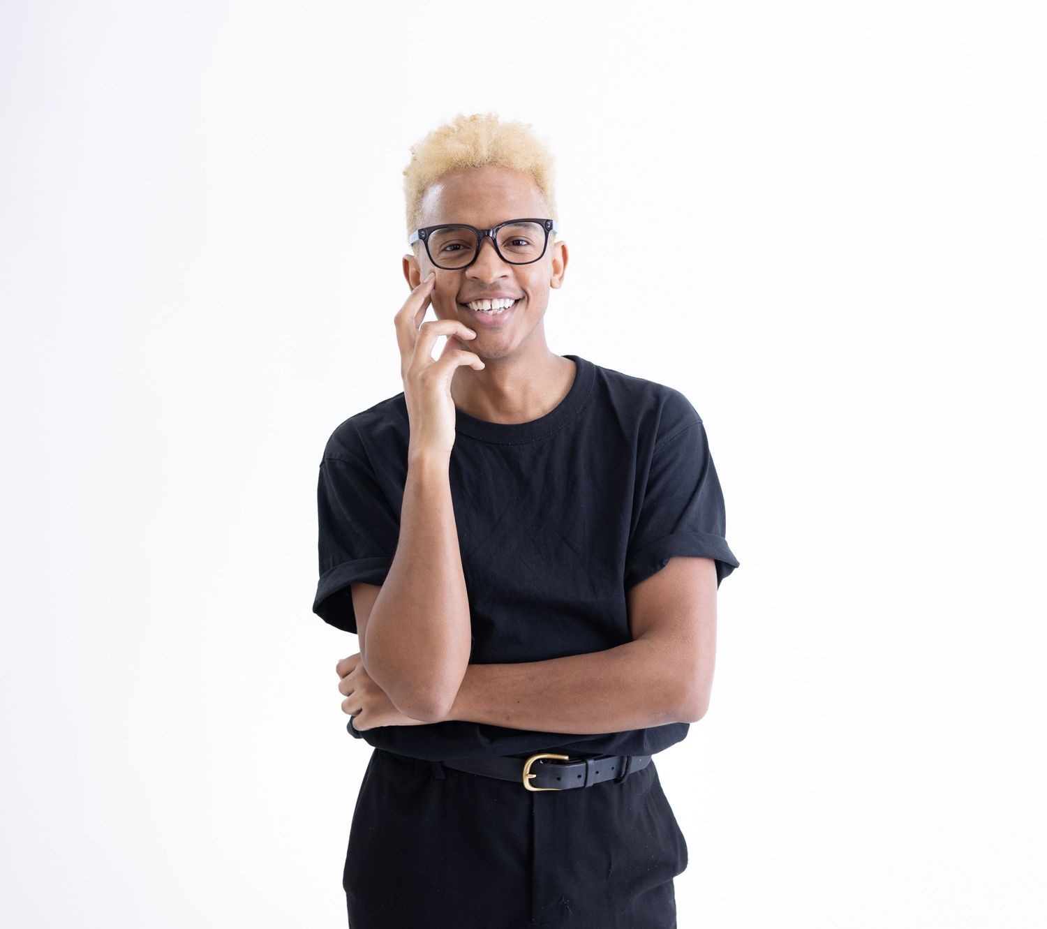 Young man with blonde hair wearing glasses and black outfit smiling while talking on phone.