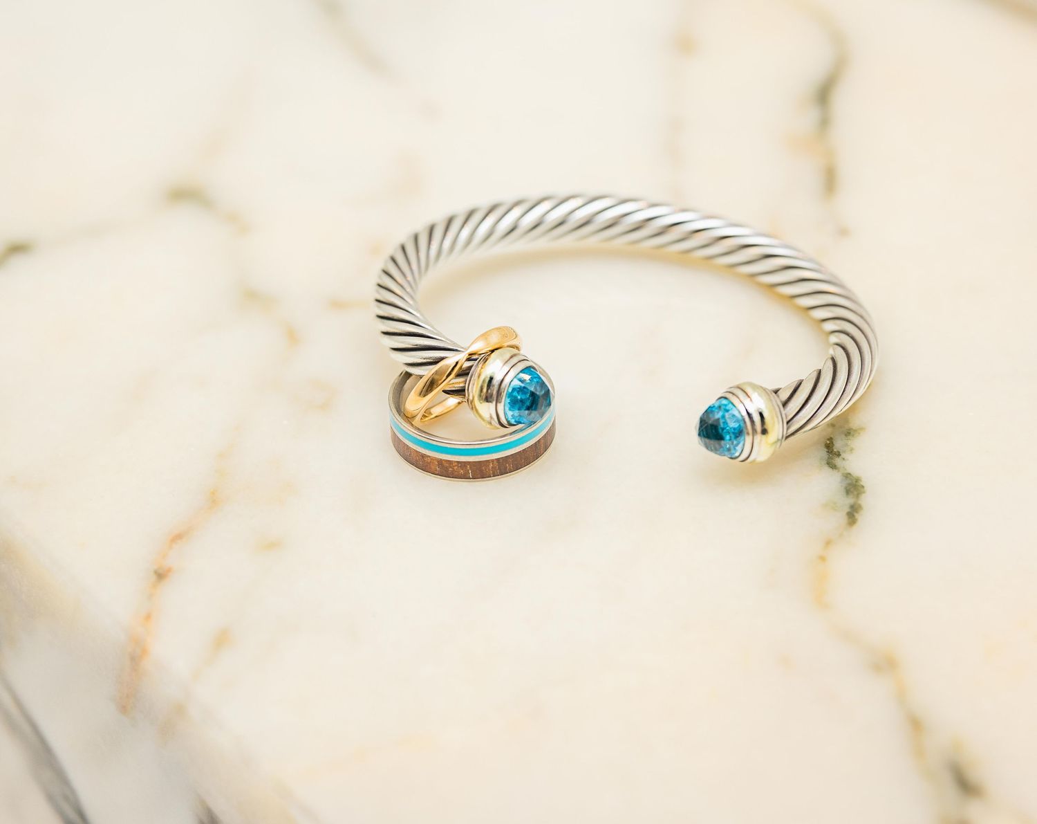 Silver and gold cable cuff bracelet with blue topaz gemstones on marble surface.