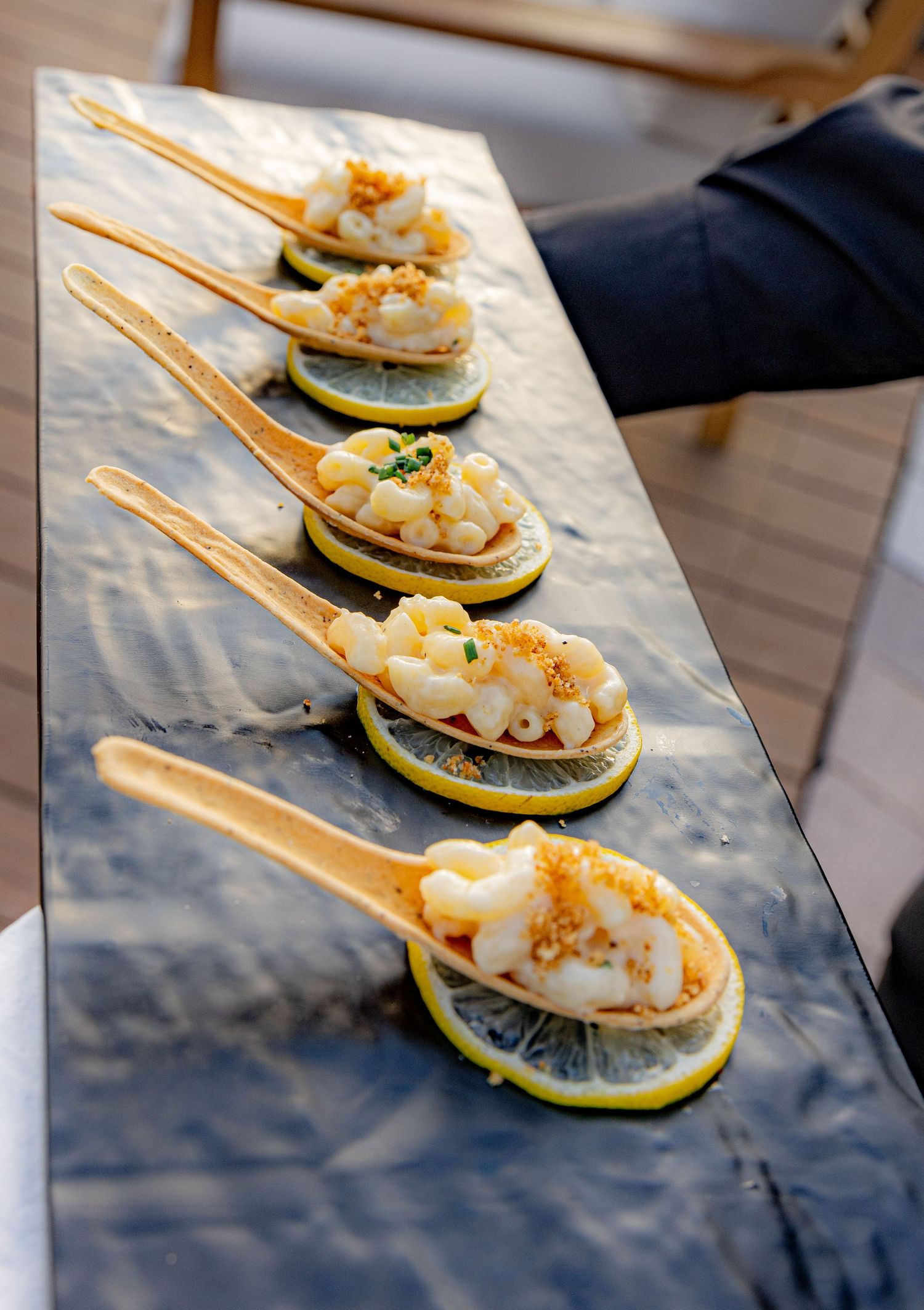 Five wooden spoons with creamy seafood appetizers resting on lemon slices on a slate board.
