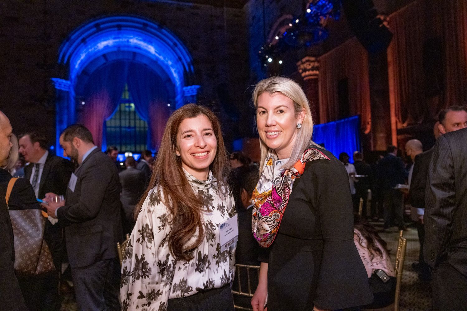 Two women smiling together at elegant blue-lit gala event venue.