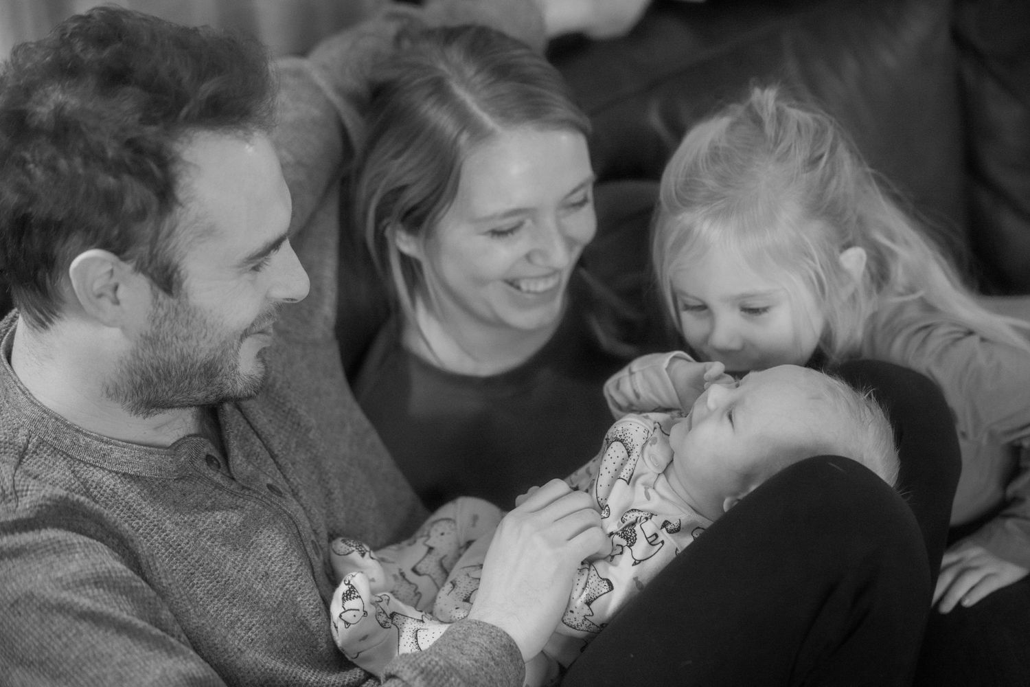 Black and white family photo of parents and two children cuddling on a sofa.