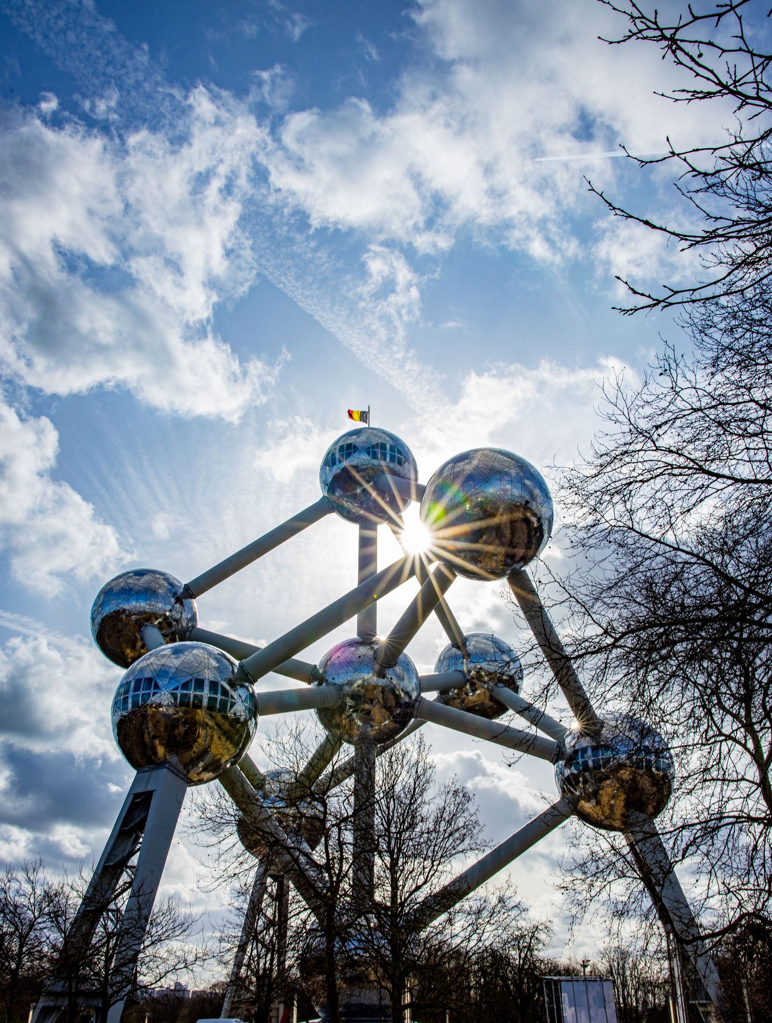 Atomium landmark in Brussels with metallic spheres gleaming against a blue cloudy sky with sun flare.