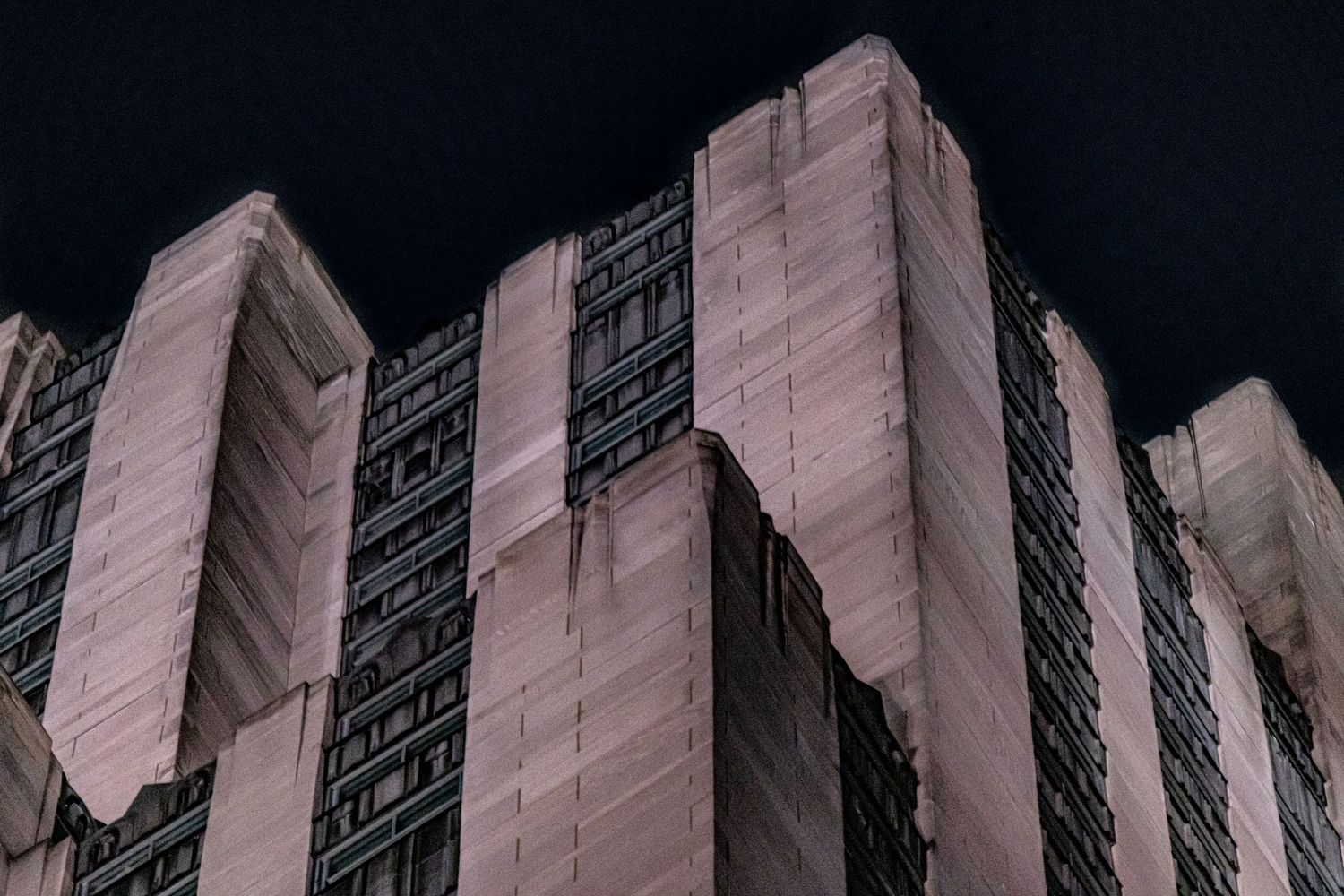 Dark dramatic low-angle shot of a brutalist concrete skyscraper facade at night.