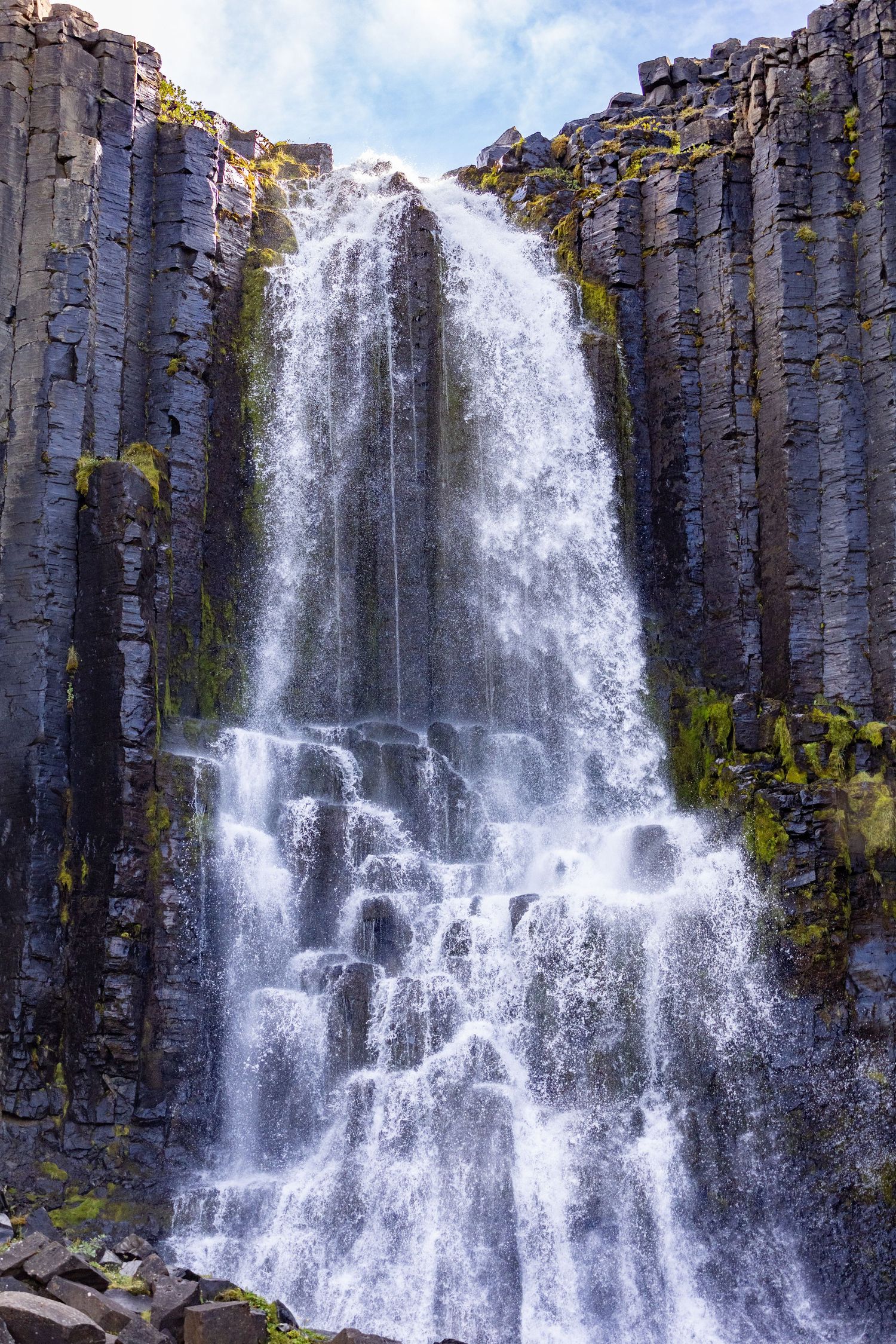 Dramatic waterfall cascading down towering basalt column cliffs covered in green moss in Iceland.