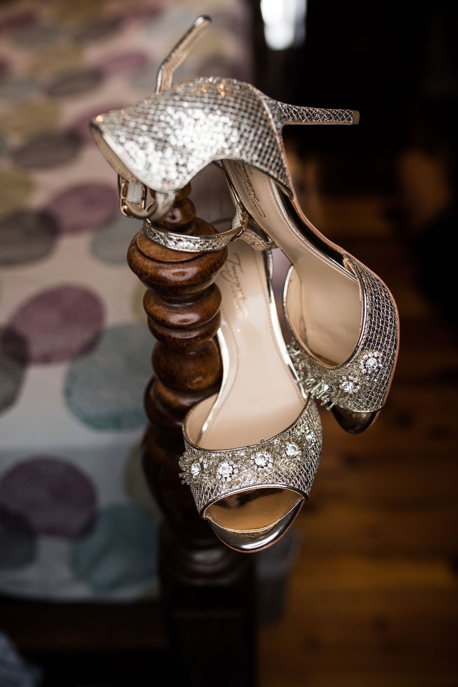 Sparkling silver embellished bridal heels hanging on a wooden chair post in a wedding venue.