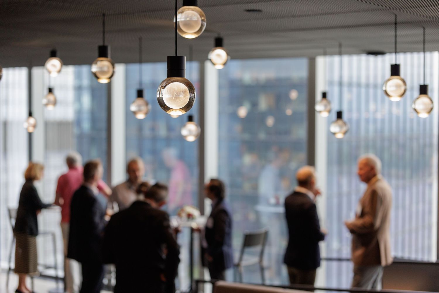Blurred silhouettes of business professionals networking in a modern office space with decorative pendant lights.