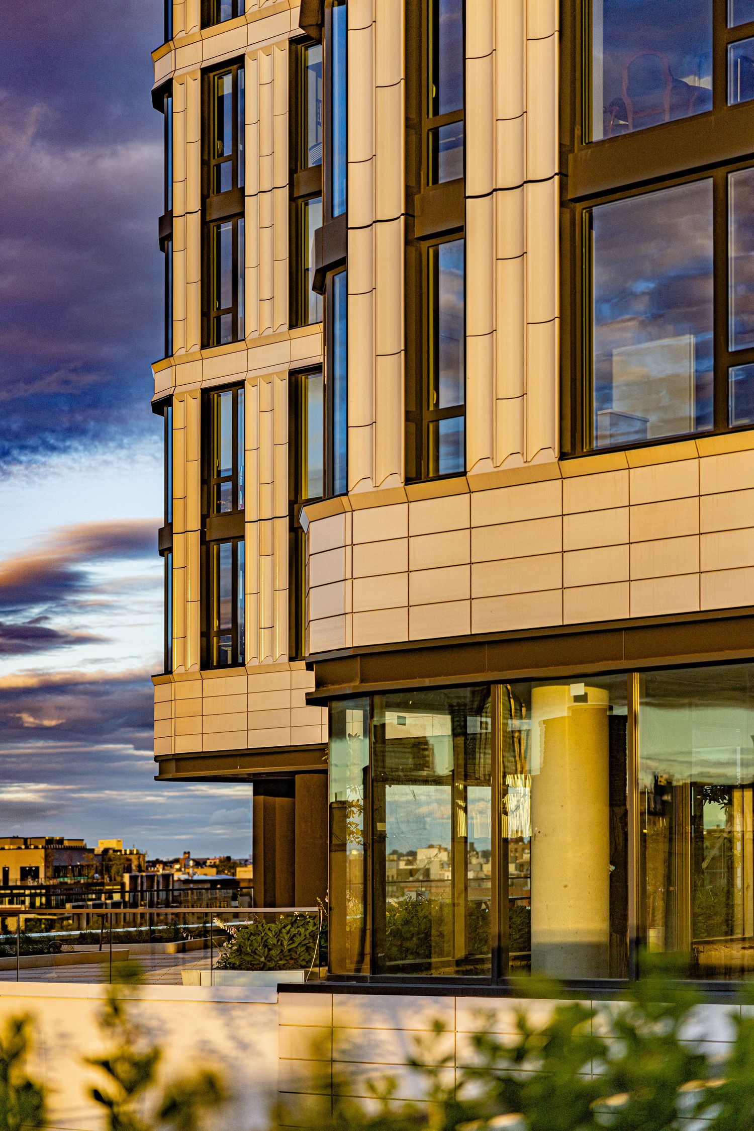 Contemporary luxury apartment building exterior detail at sunset with warm golden light on beige stone facade.