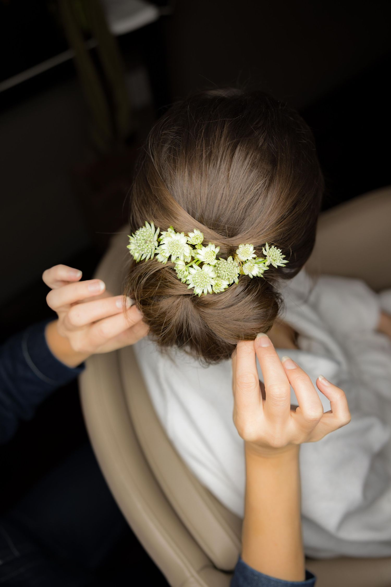 Hairstylist arranges delicate white flowers into bride's elegant updo hairstyle before the wedding ceremony.