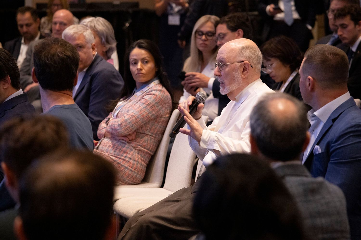 Audience members listening attentively as elderly man speaks into microphone at a professional conference.