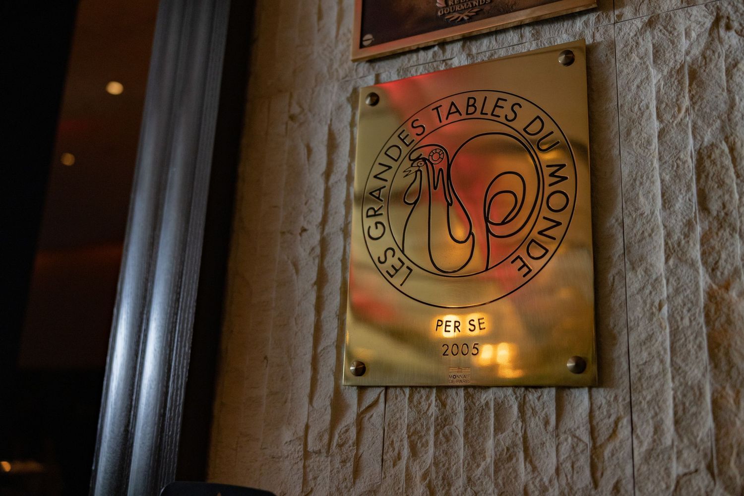 Gold brass plaque for Les Grandes Tables du Monde at Per Se restaurant mounted on stone wall.