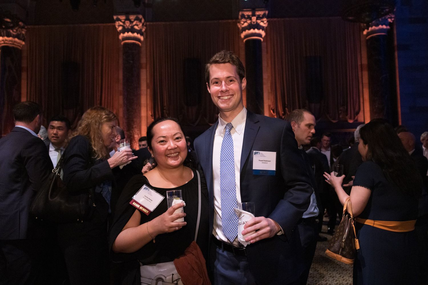 Man and woman posing together at corporate networking event with name badges.