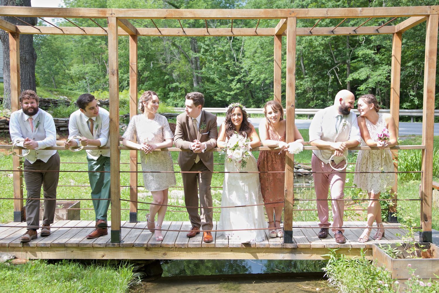 Wedding party poses together on a wooden bridge pergola surrounded by nature at an outdoor wedding.