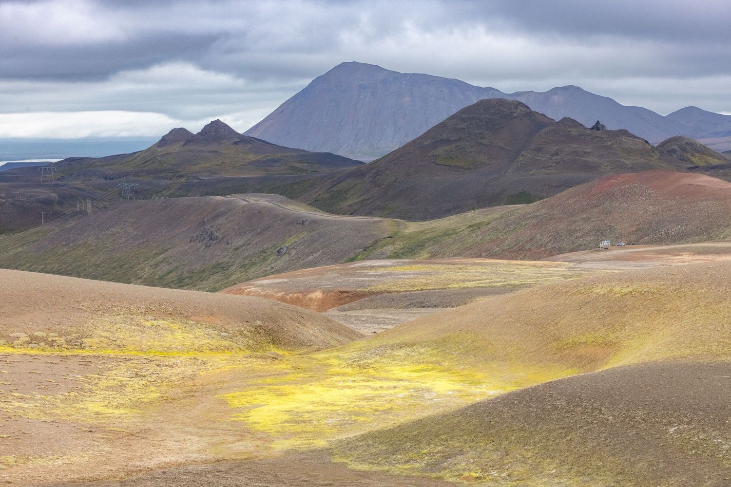 A vast colorful volcanic highland landscape with yellow sulfur deposits and rust-colored hills under an overcast sky in Iceland.