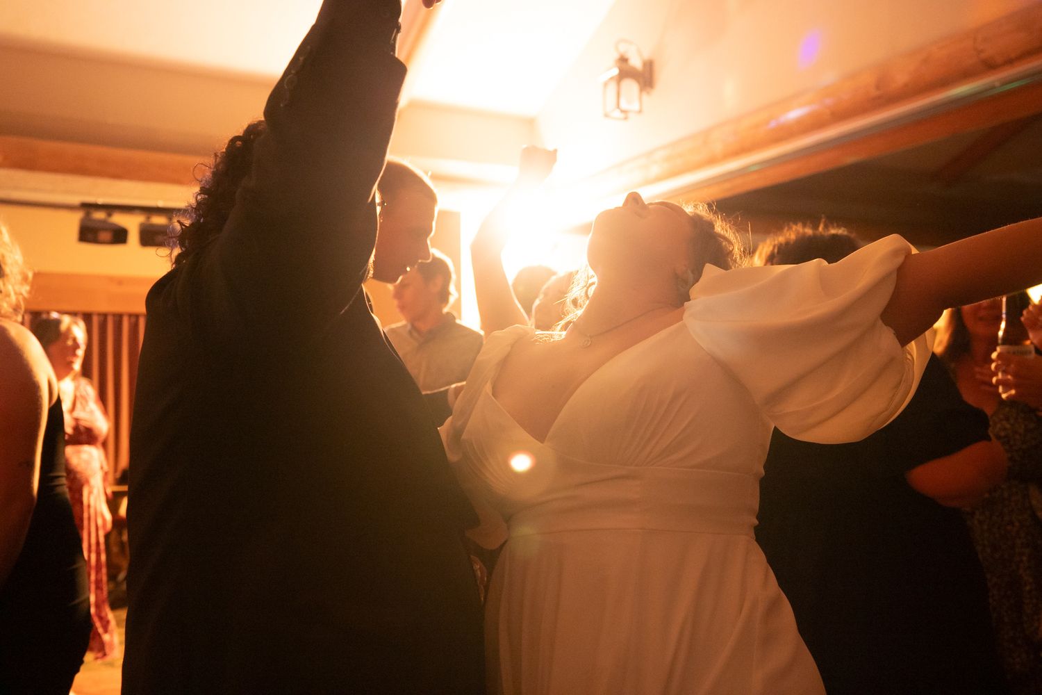 Bride and guests dancing joyfully under warm golden lights at an energetic wedding reception celebration.