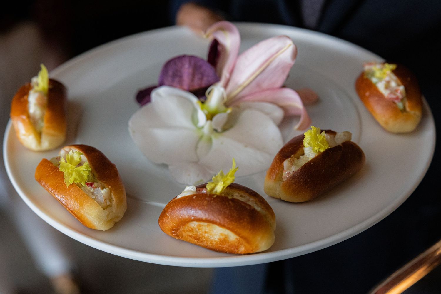 Elegant appetizer plate with six brioche rolls garnished with herbs and a pink flower centerpiece.