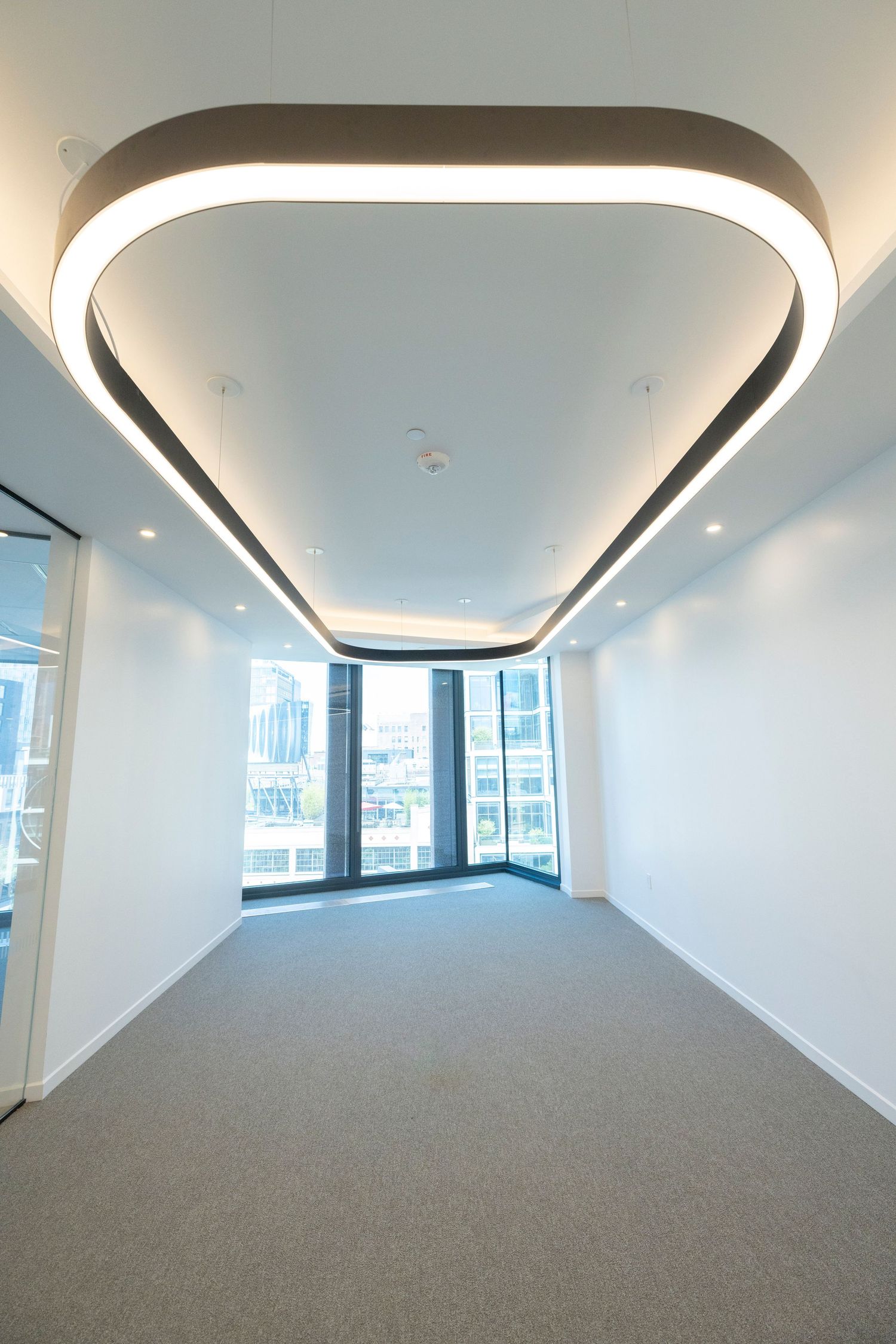 Empty modern office space with unique triangular LED ceiling light fixture and floor-to-ceiling city view windows.