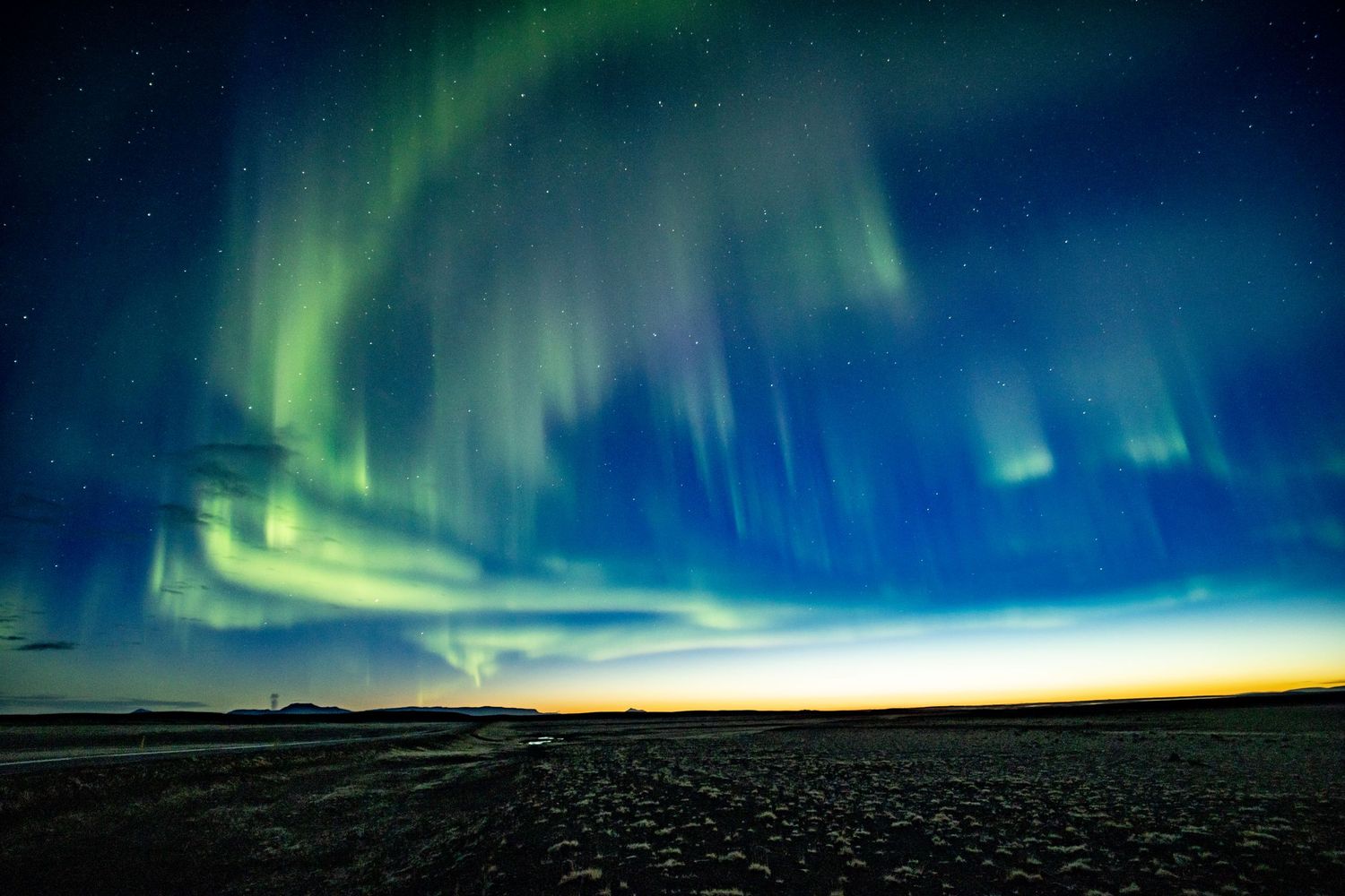 Vibrant green and blue aurora borealis northern lights illuminating the night sky over flat terrain.