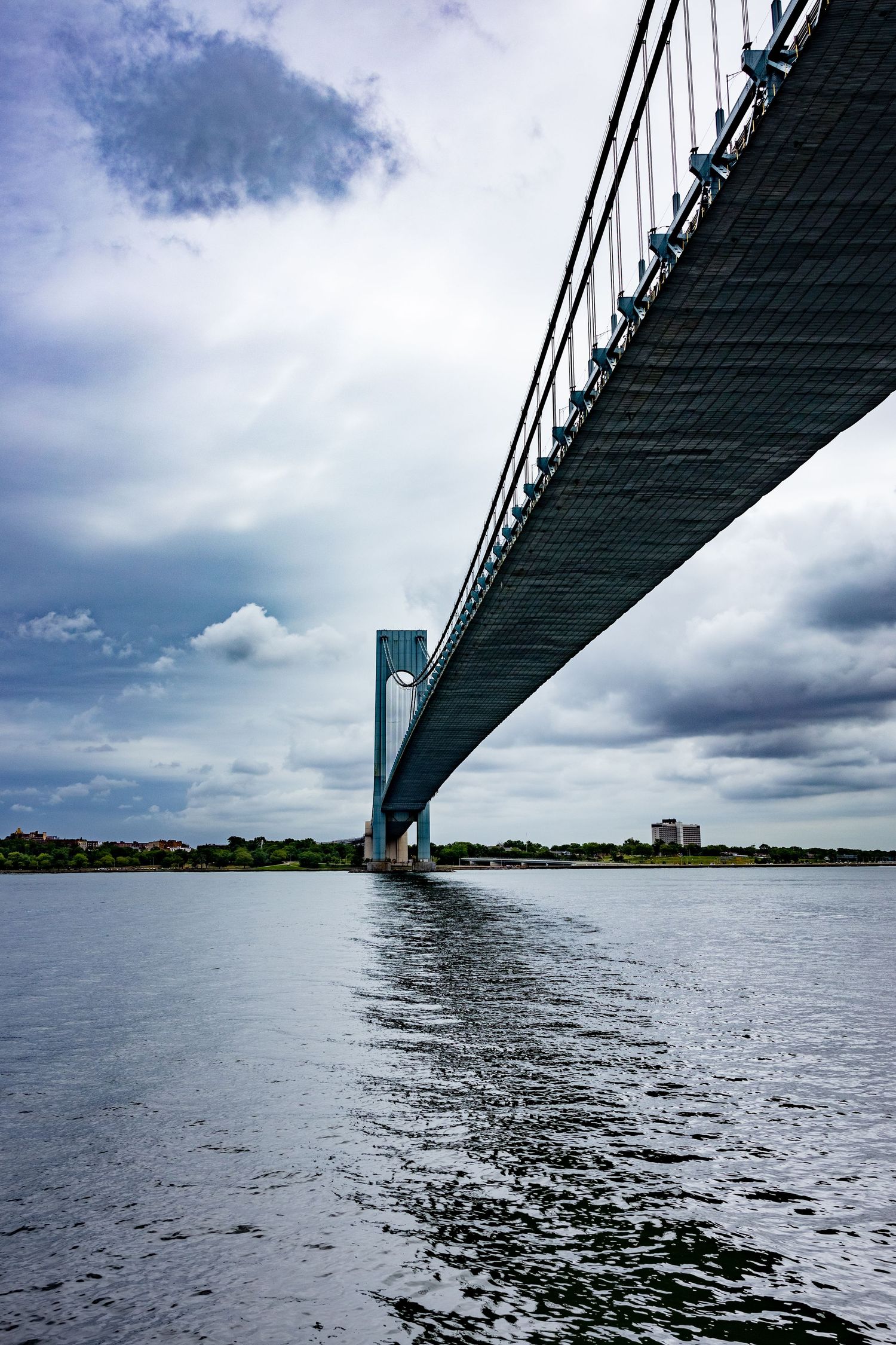 Verrazano-Narrows Bridge viewed from below over calm water with dramatic cloudy sky in New York.