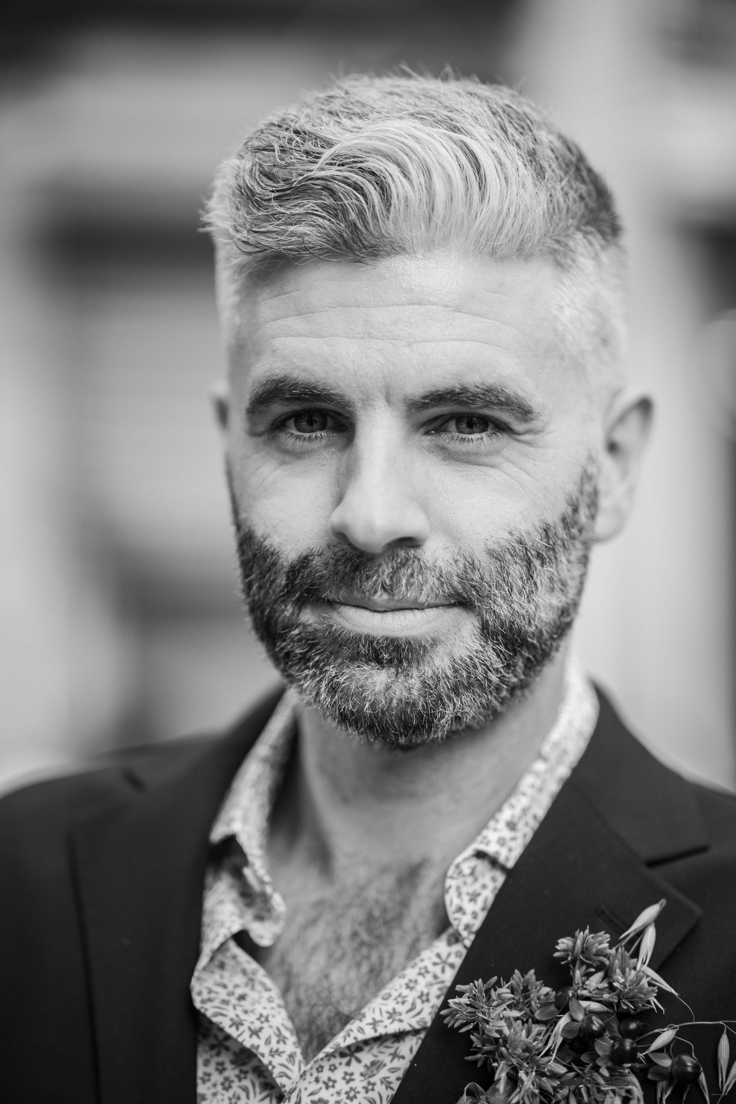Black and white portrait of mature bearded white man with gray hair wearing blazer with boutonniere.