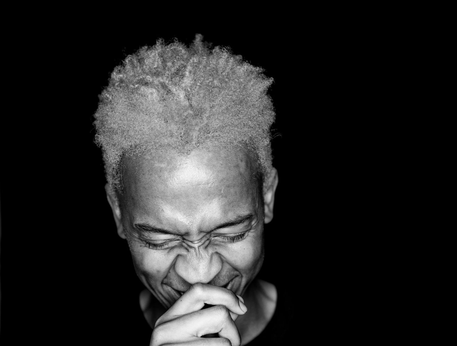 Black and white portrait of a person laughing with hands clasped near face.