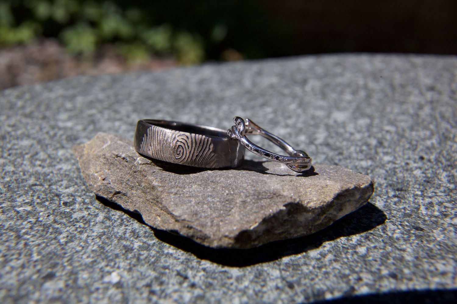 Two wedding rings, one with fingerprint engraving and one diamond, displayed on a stone surface.