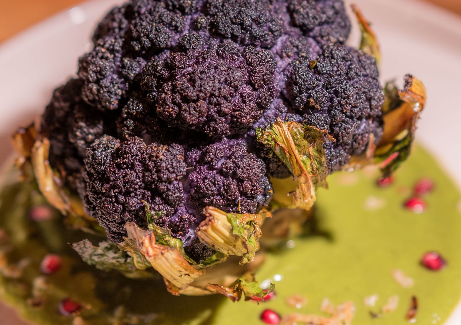 Roasted purple cauliflower served on vibrant green sauce garnished with pomegranate seeds.