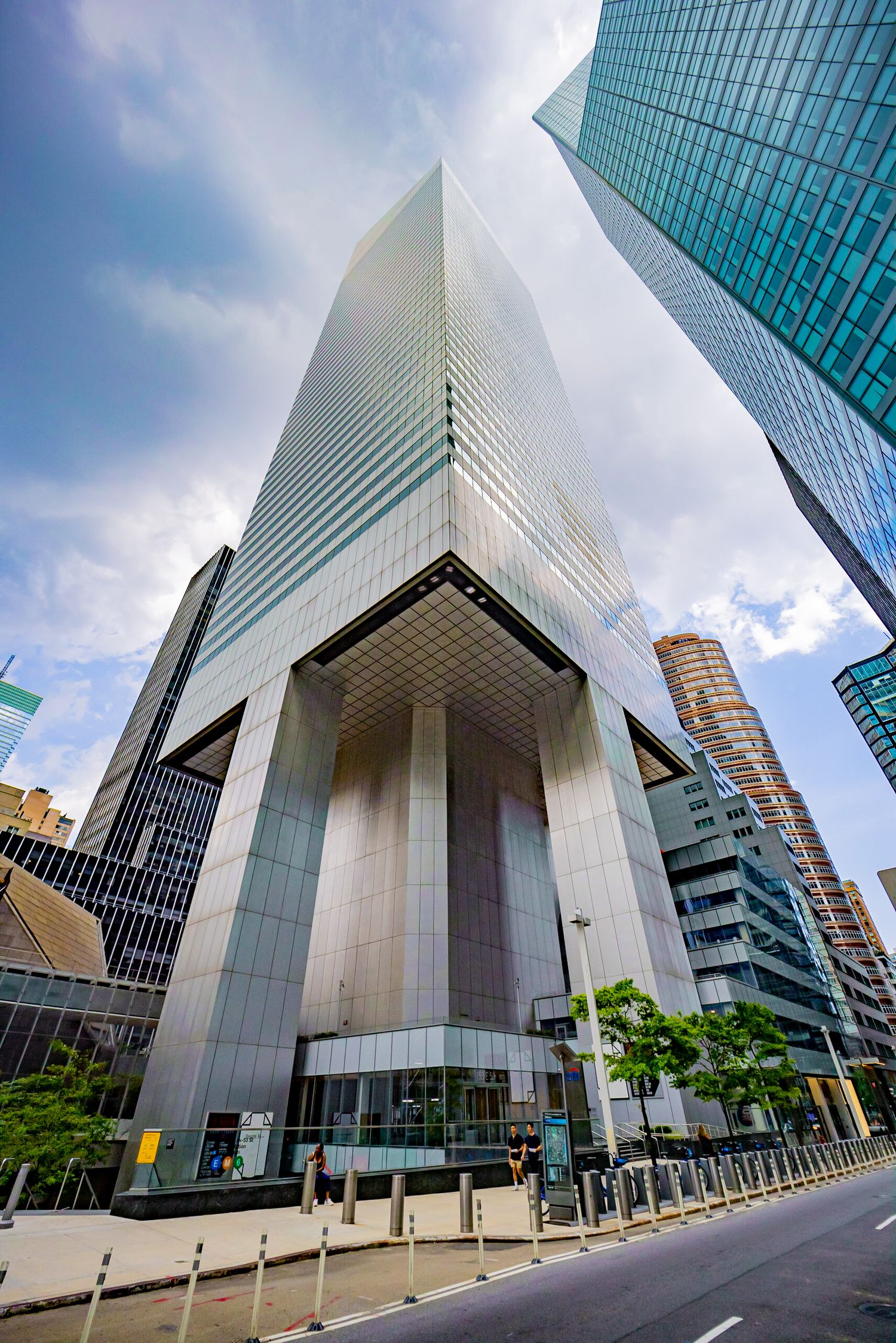Low-angle view of a massive silver glass skyscraper with a dramatic arched entrance on a city street.