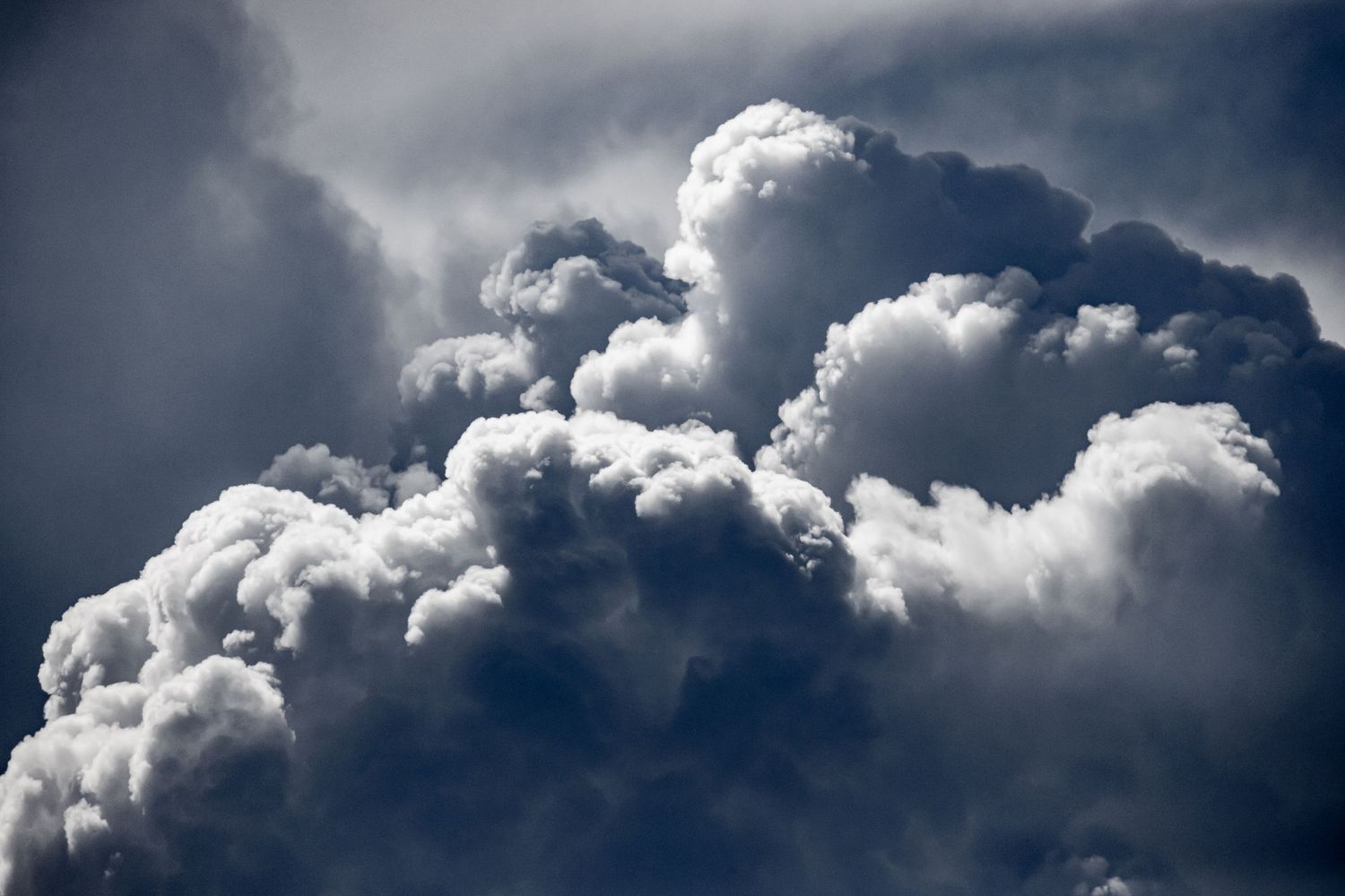 Dramatic dark storm clouds billowing and building against a deep blue sky.