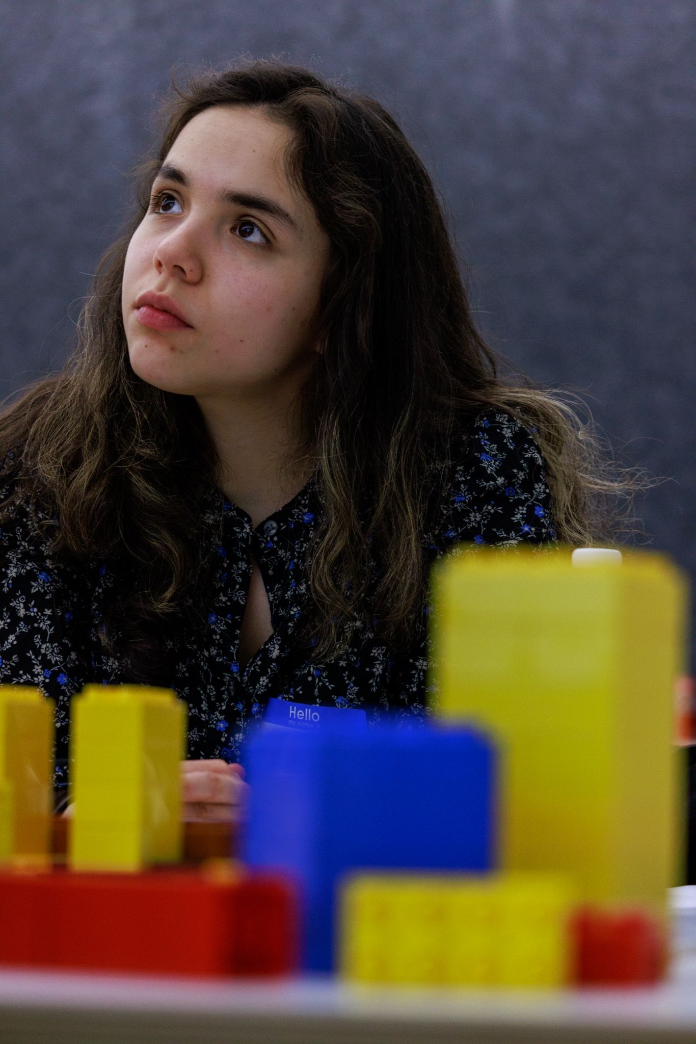 A young woman with long dark hair gazes upward thoughtfully during a LEGO workshop activity.