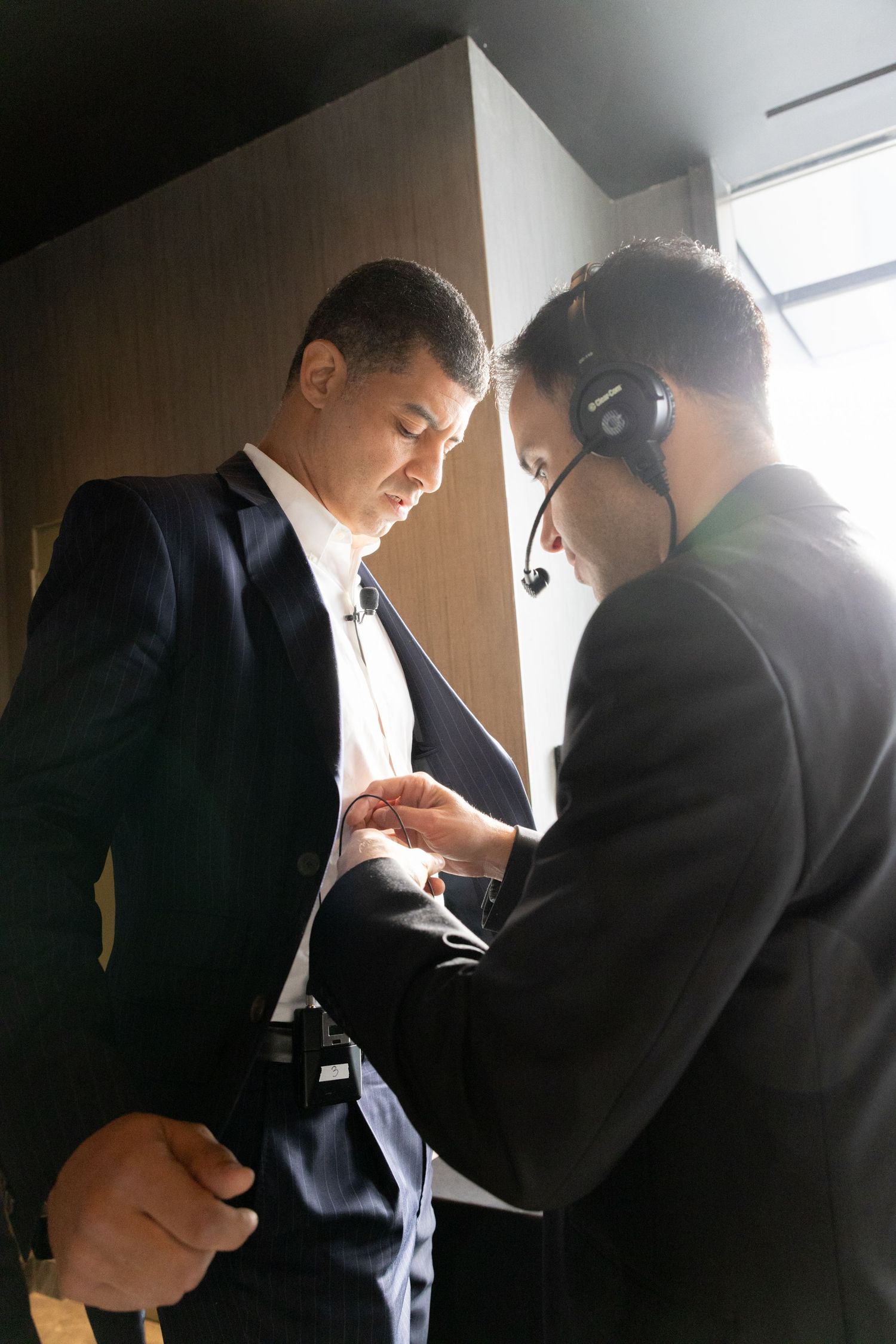 A technician with headset adjusts a mans suit jacket before a professional event or conference.