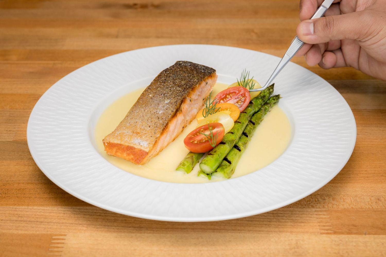 Pan-seared salmon fillet served with asparagus, cherry tomatoes, and creamy butter sauce on a white plate.