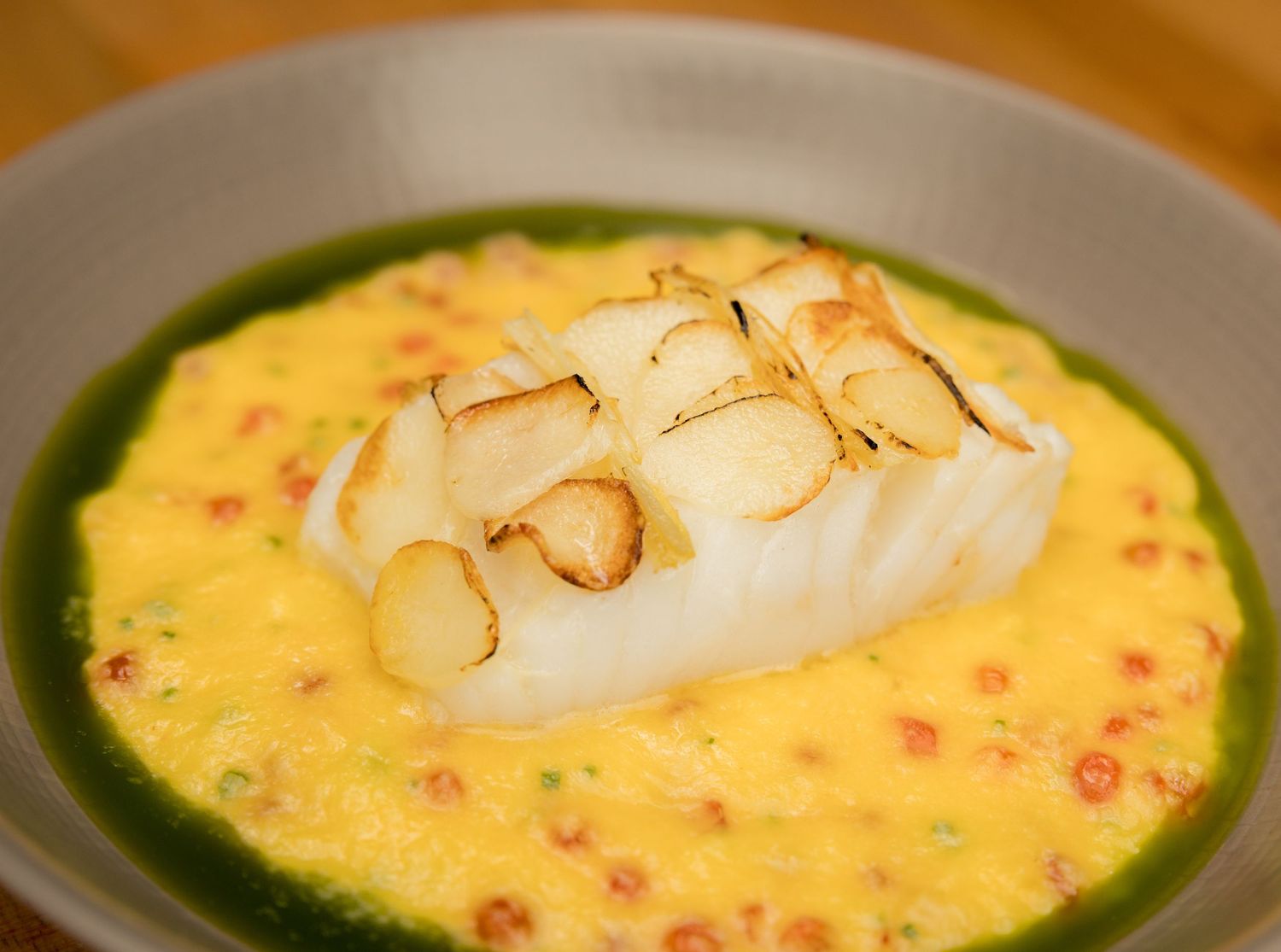 Pan-seared white fish fillet served over creamy yellow sauce with green herb oil in a bowl.