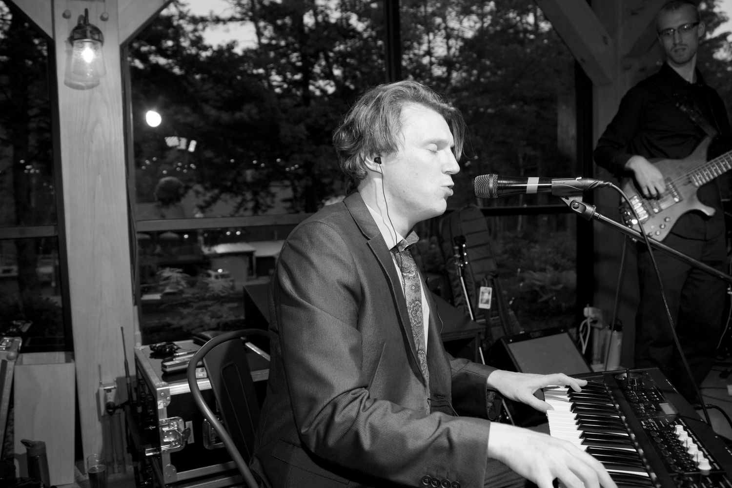 Male musician playing keyboard organ on stage at wedding reception in black and white photography.