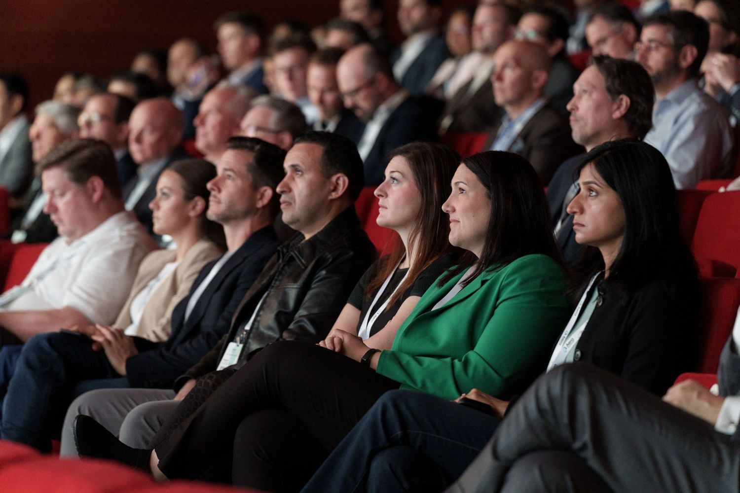Audience members seated in red chairs attentively watching presentation at conference.